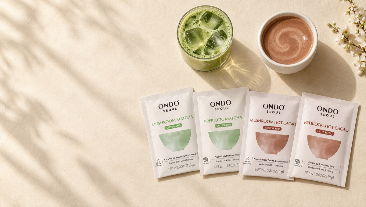 Four ONDO° latte sample sachets beside an iced matcha latte and a cup of hot cacao.