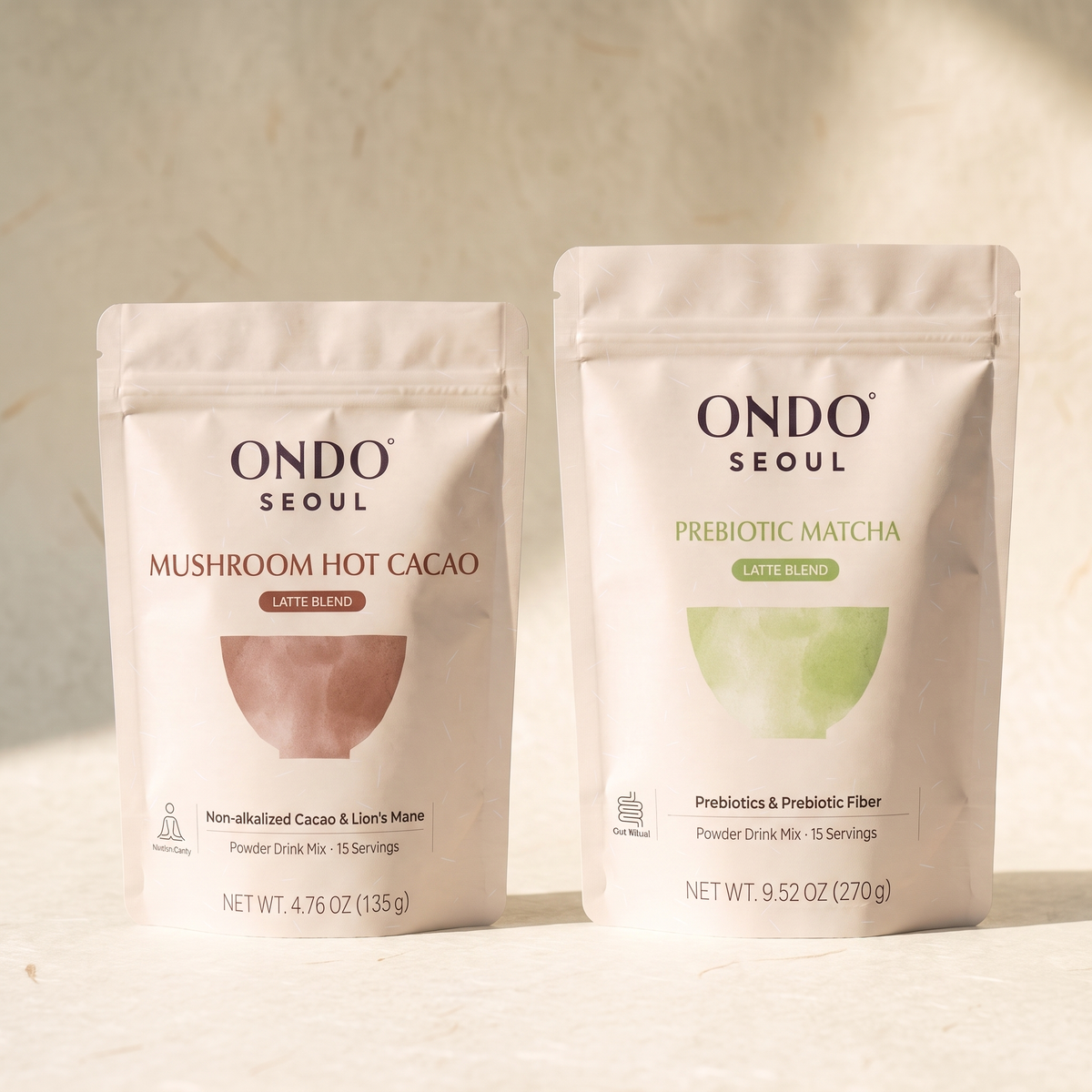 The Long Day Duo: two pouches, Prebiotic Matcha Latte Blend and Focus Mushroom Hot Cacao Latte Blend, on ivory hanji paper.