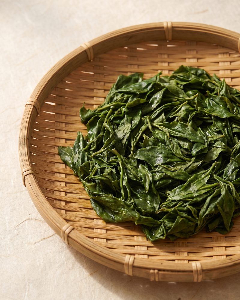 Bright green steamed tea leaves on a bamboo tray