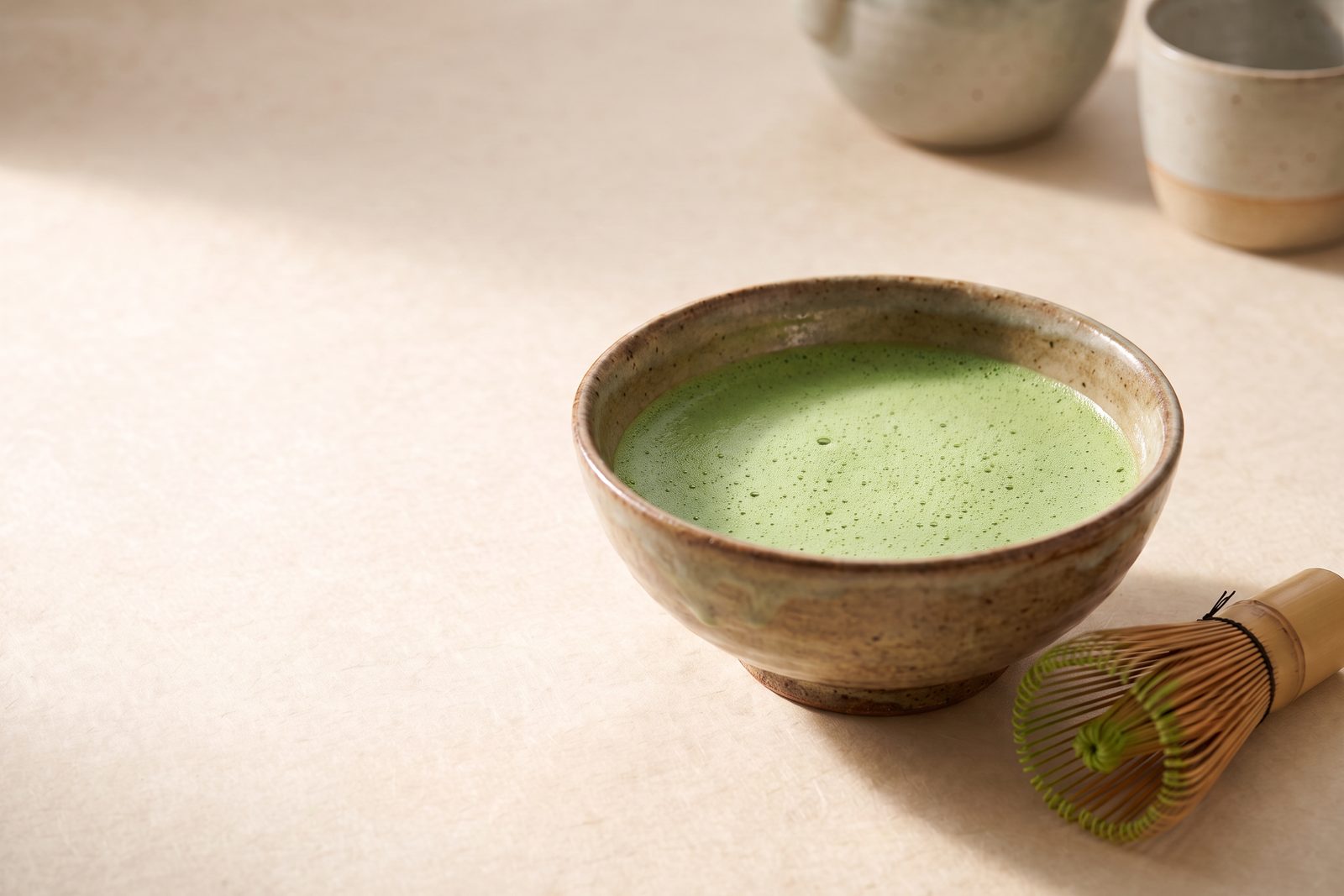 A ceramic bowl of freshly whisked matcha with fine green foam, a bamboo whisk beside it